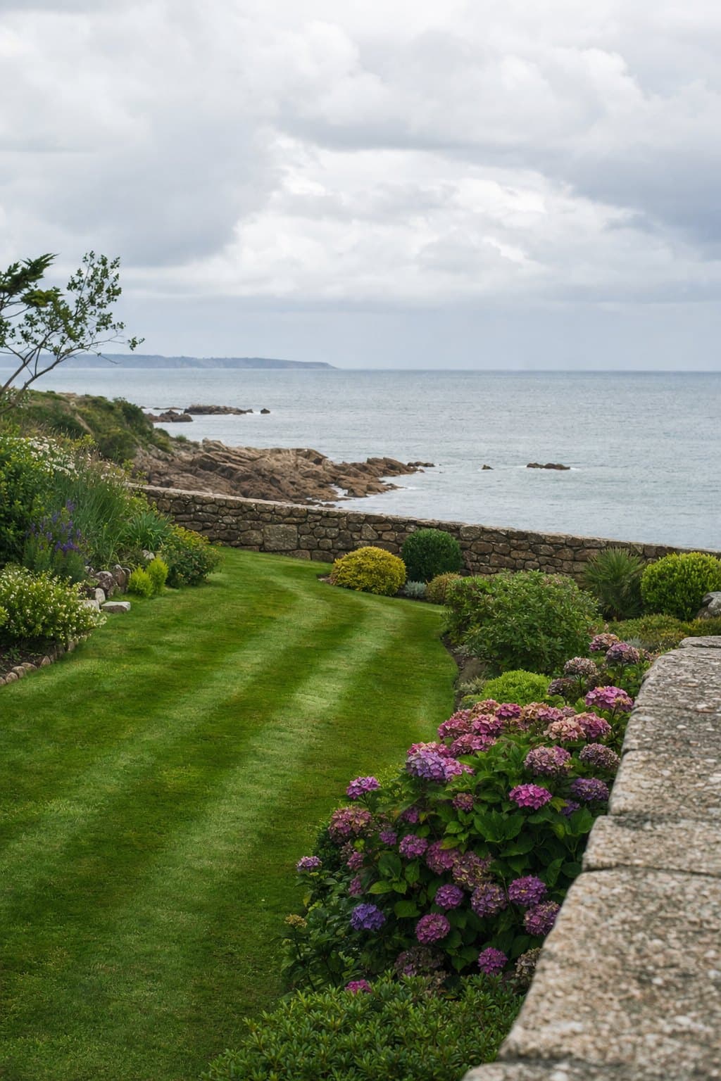 Un jardin de bord de mer breton entretenu, pelouse tondue, hortensias et muret de granit