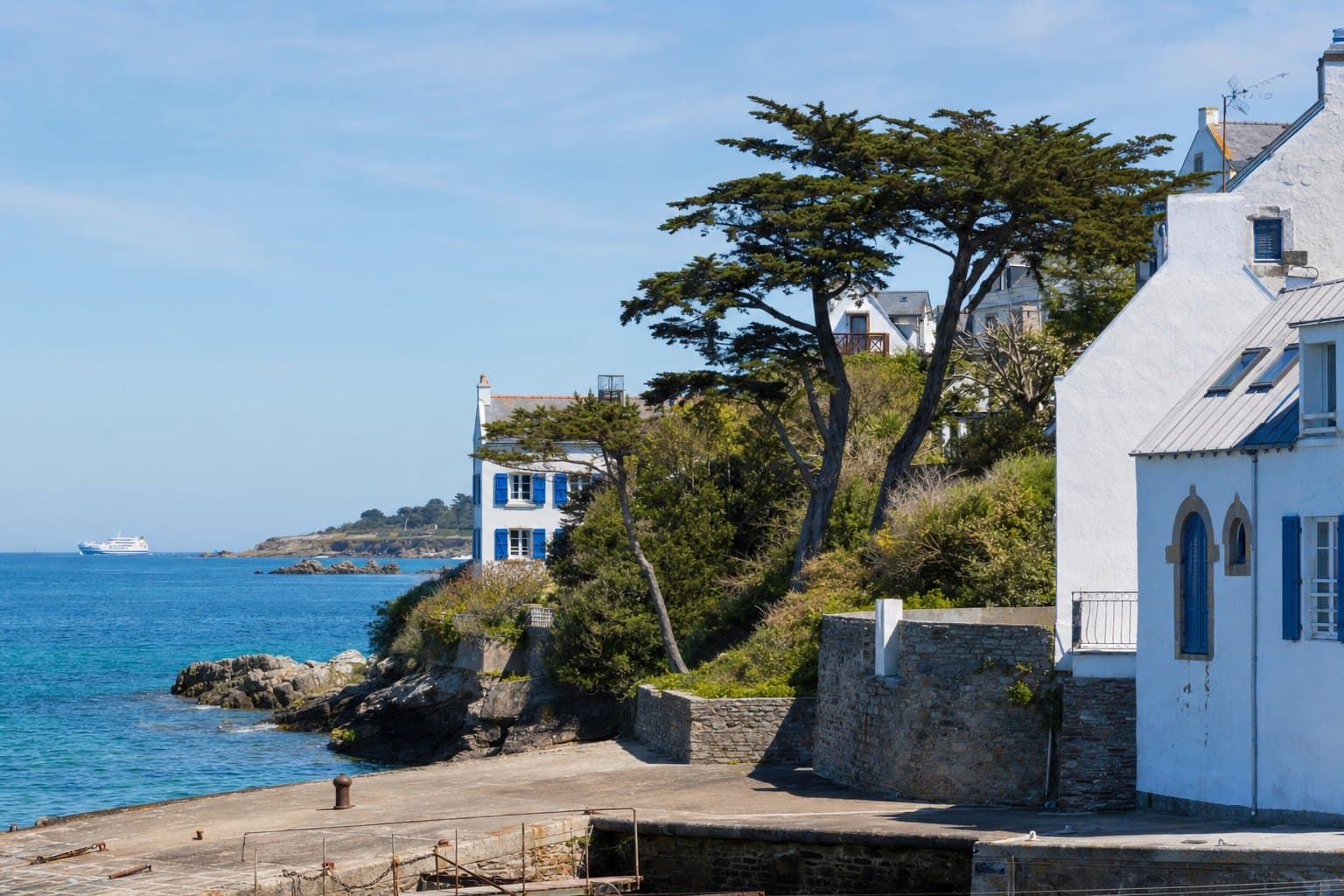L'île de Groix vue depuis Port-Tudy, maisons blanches, pins et cyprès courbés par le vent au-dessus des jardins