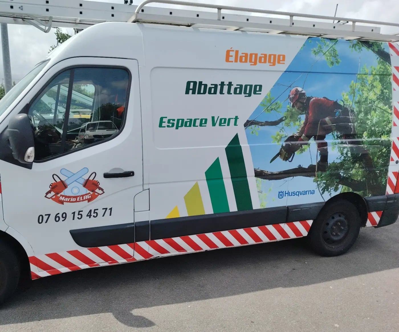 Le camion blanc de Mario Élag, flanc marqué élagage, abattage, espace vert, garé devant un jardin