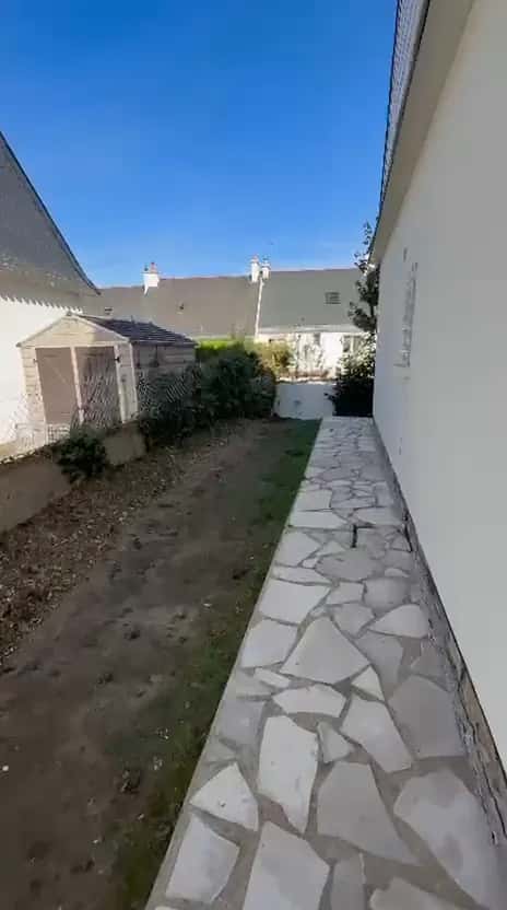 Allée dallée le long d'une maison, terre nettoyée et grillage dégagé jusqu'au cabanon
