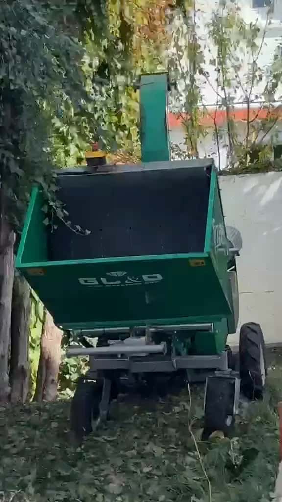 Broyeur de végétaux vert installé au fond du jardin, entre les arbres