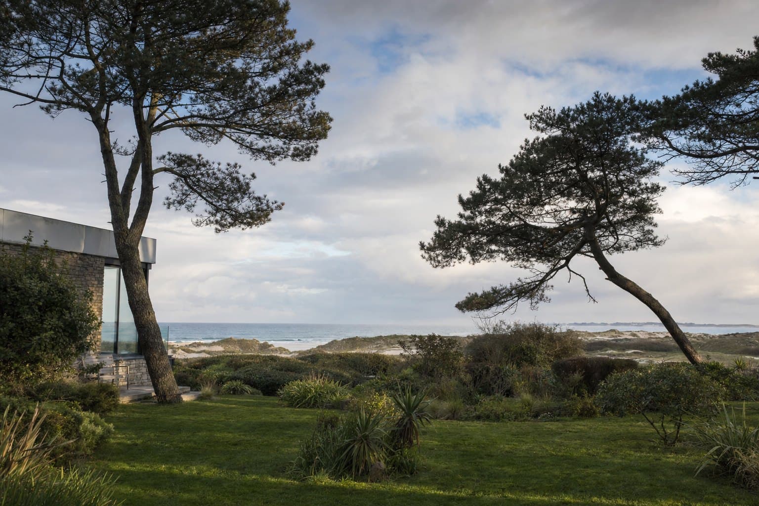 Un jardin de villa près de la côte à Ploemeur, pins maritimes courbés par le vent, mer au loin